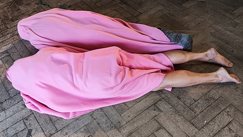 Zwei Personen unter rosa Fleecedecken liegen auf dem Boden. Man sieht nur die nackten Beine und Füße.