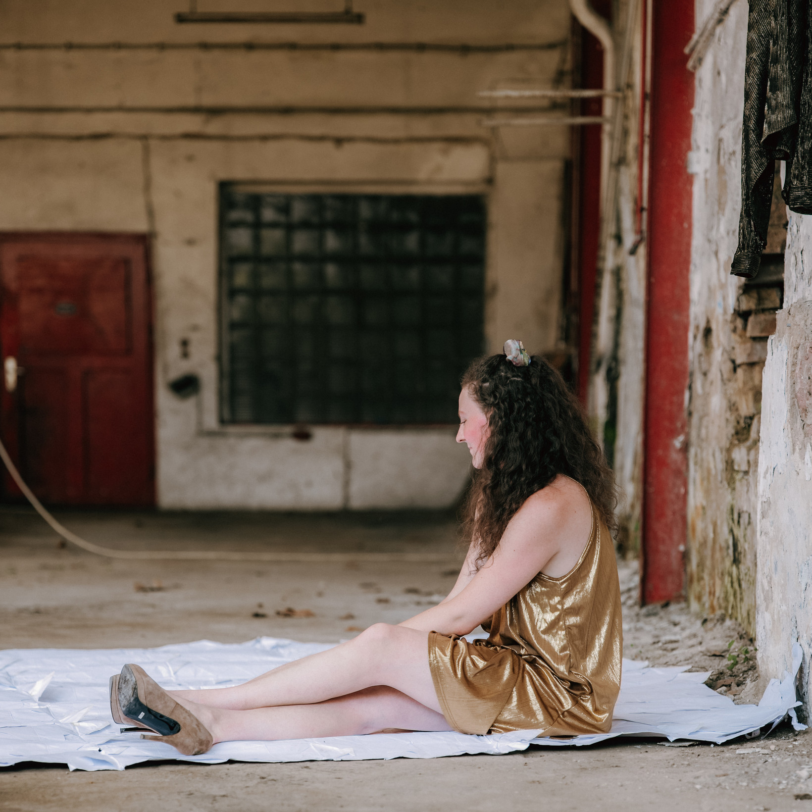 Person im goldenen Kleid sitzt auf einem weißen Laken auf dem Boden der Halle hinter zeitraumexit