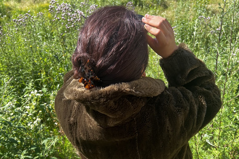 Frau steht im Pelzmantel auf der Wiese und schaut durch ein Fernglas