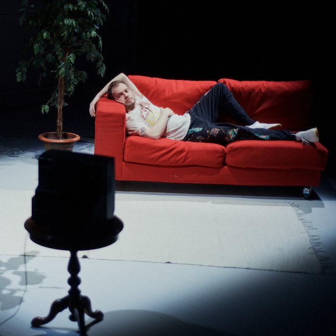 Person liegt auf einem roten Sofa und schaut in Richtung eines Röhrenfernsehers.