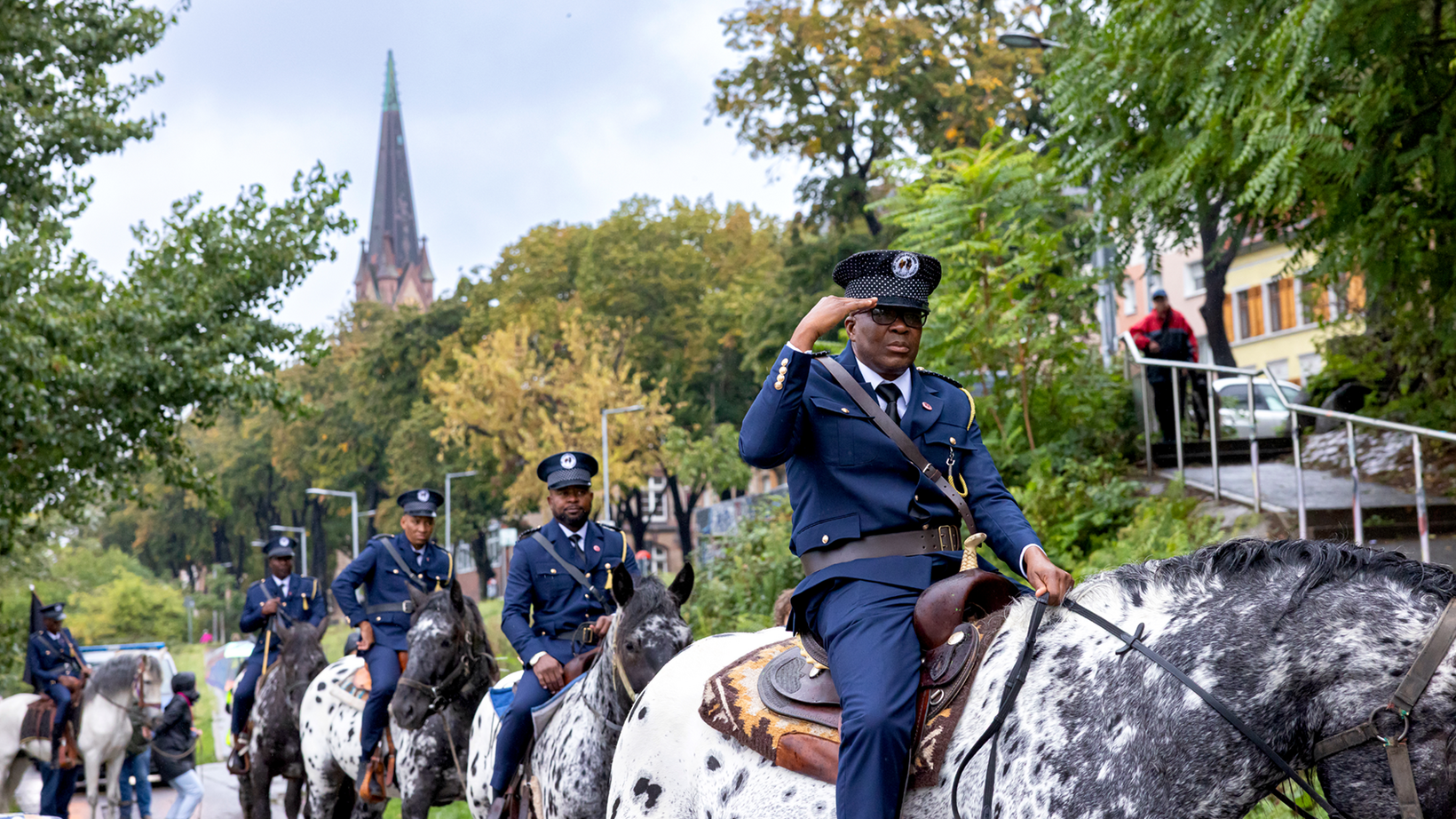 Persons wearing military uniforms riding on horseback along the shore of the Neckar