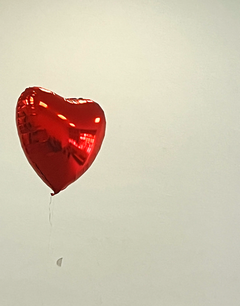 roter Herzluftballon schwebt vor einer weißen Wand