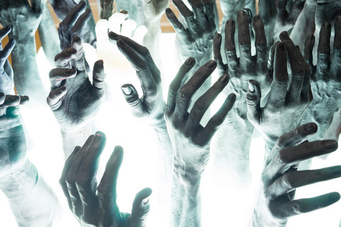 Aus einem weiß leuchtenden Boden ragen graue Hände in die Luft