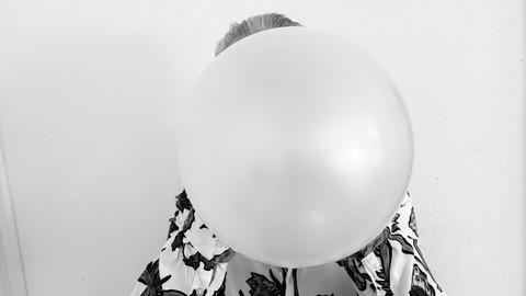 Person pustet einen Luftballon auf. Das gesamte Gesicht ist vom Ballon verdeckt