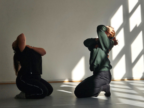 Zwei Personen knien sich in einem Raum gegenüber und halten ihre Köpfe