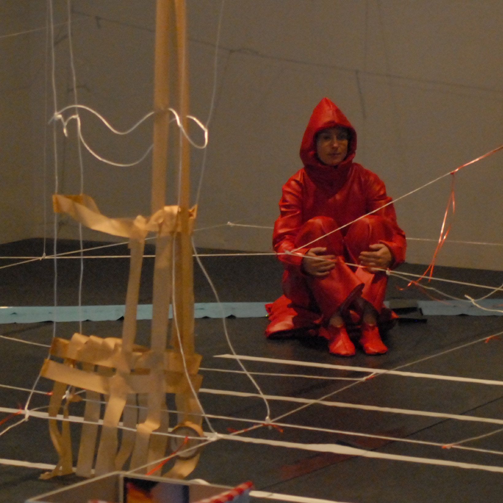 Eine Person in orangener regenkleidung sitzt in einem Raum in dem Schnüre gespannt sind