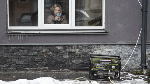 Person fotografiert mit Handy aus einem Haus auf die Straße. Vor dem Haus steht ein Generator