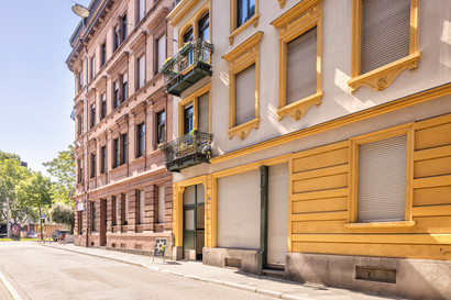 Der Eingang von zeitraumexit von der anderen Straßenseite. Das Foto zeigt ein gelbes Haus mit grüner Tür, das seitlich von rechts aufgenommen wurde.