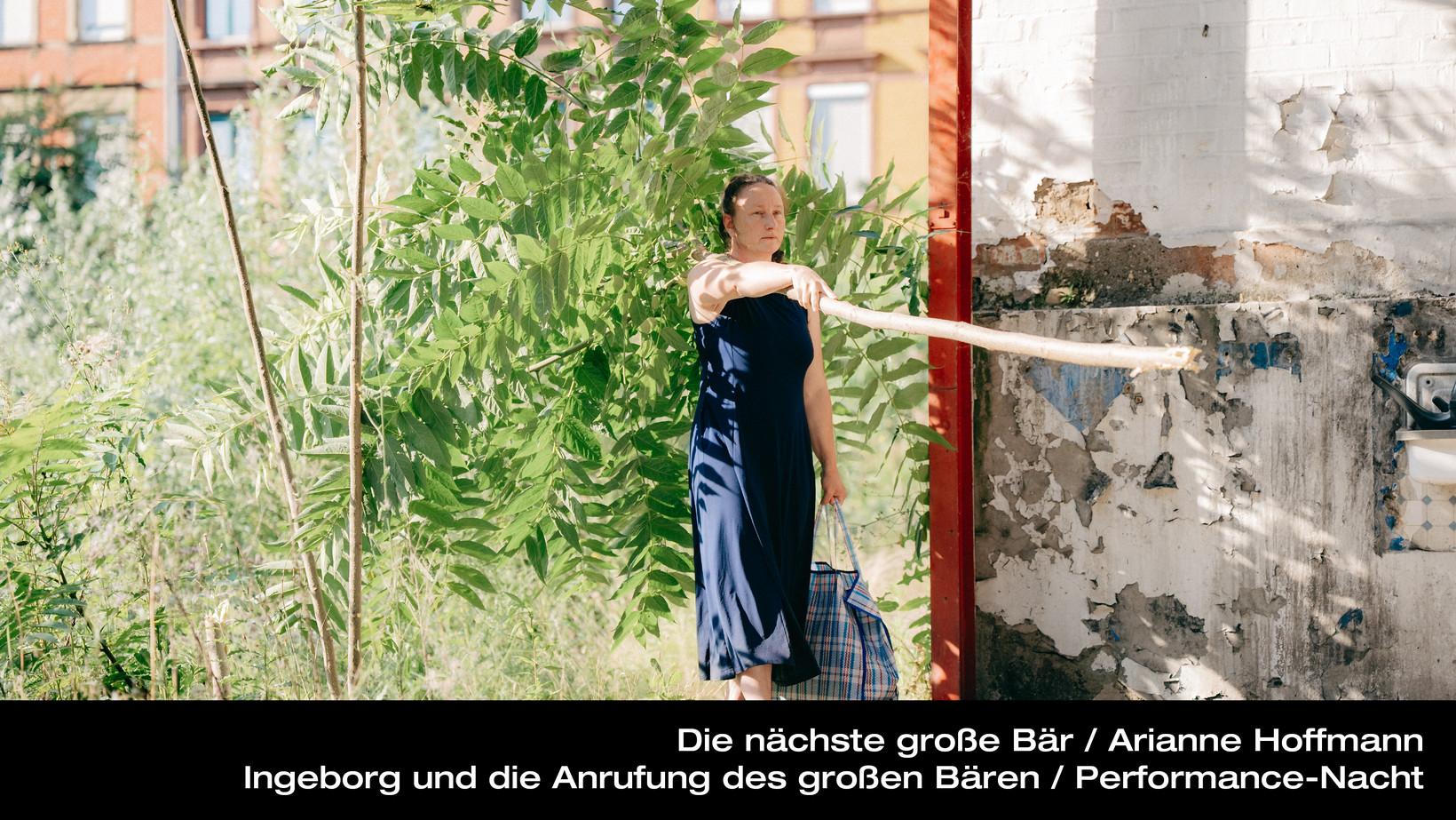 Person läuft aus der Brache in einen offenen Raum, sie hält einen großen Ast in der Hand