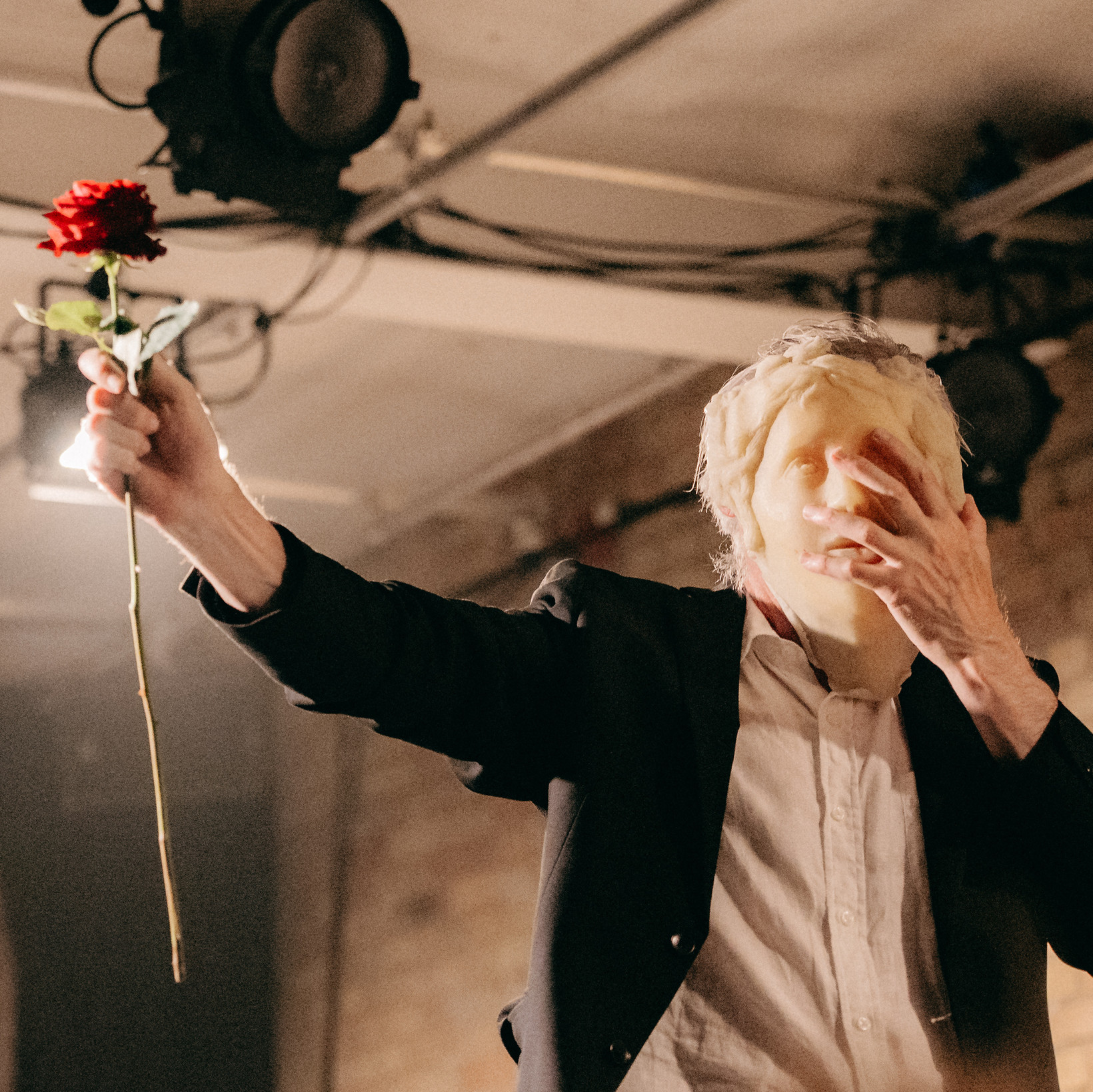 Person mit Gummimaske auf dem Gesicht, hält eine Rose in der Hand