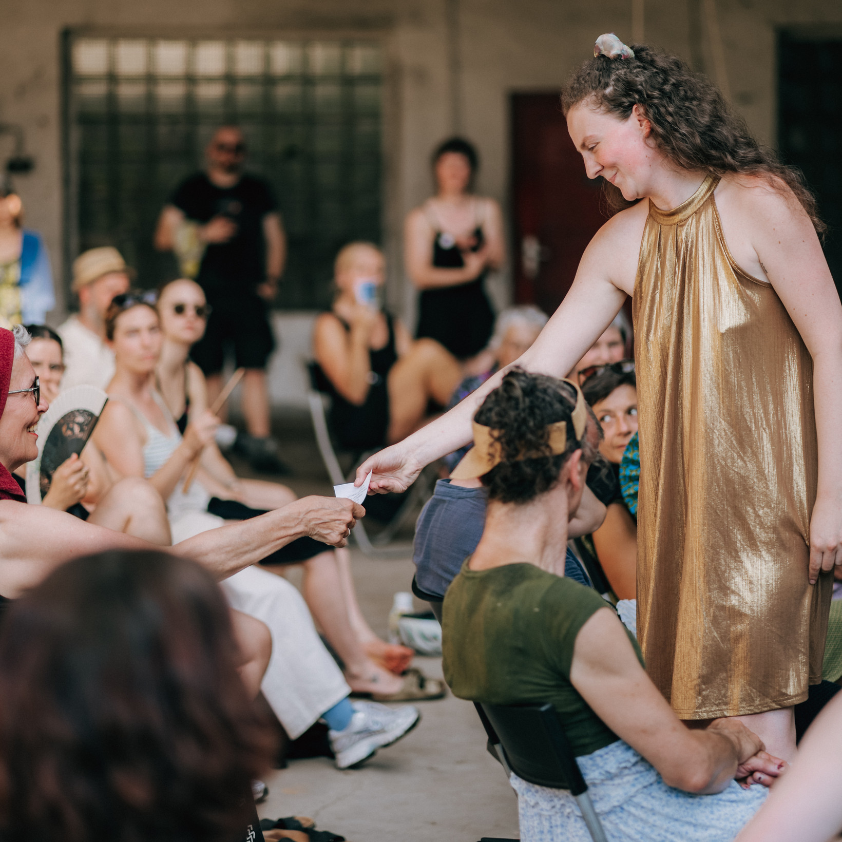 Person in goldenem Kleid reicht jemandem aus dem Publikum etwas