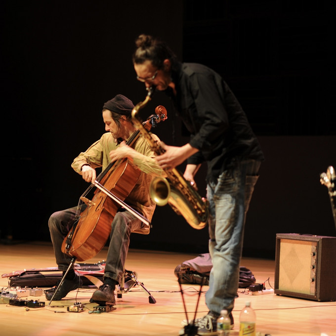 Eine Person am Saxophon und eine Person am Cello machen Musik auf einer Bühne