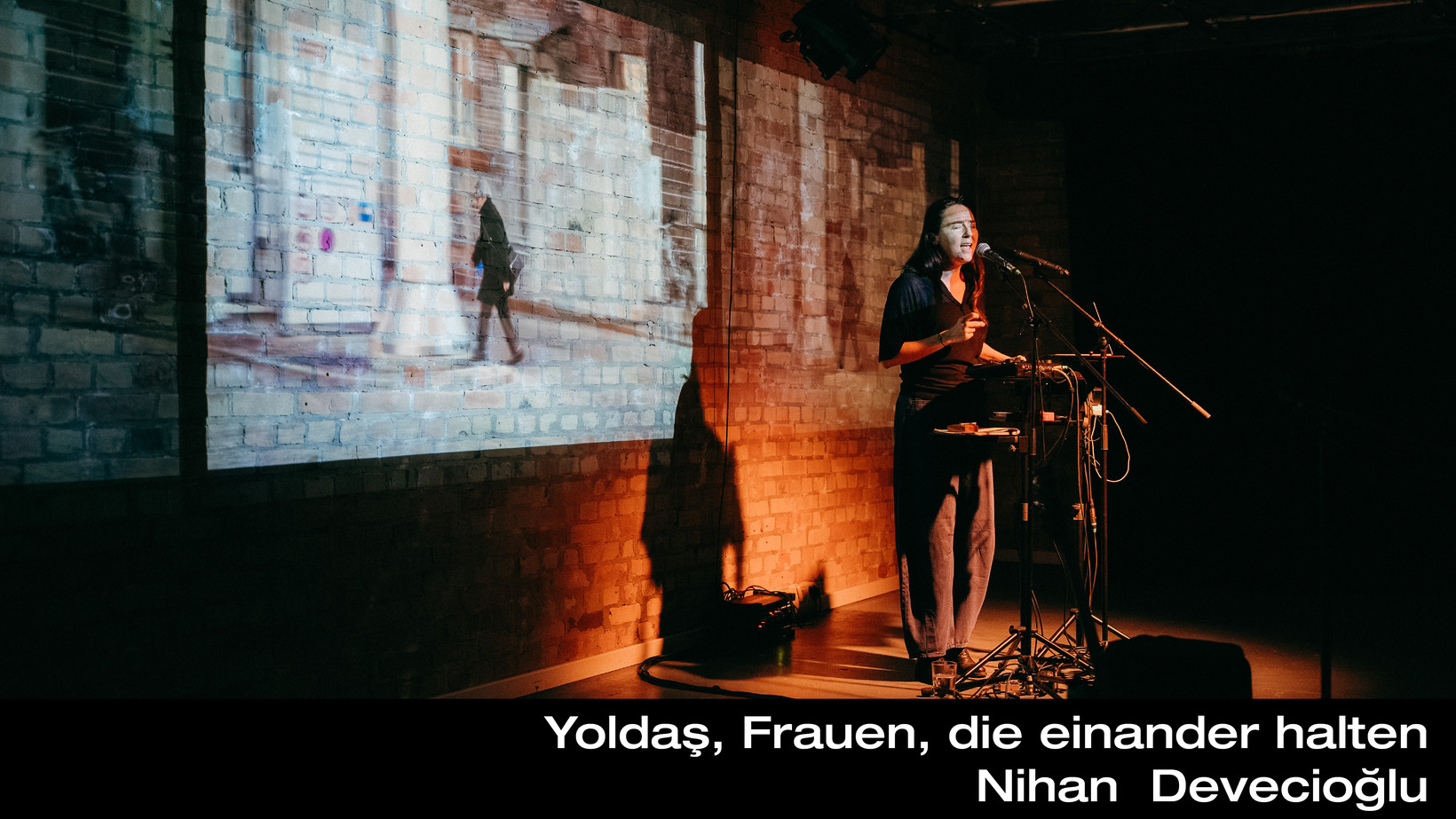 Person steht an einem Pult vor einer Backsteinmauer, auf die 3x nebeneinander ein foto projiziert ist