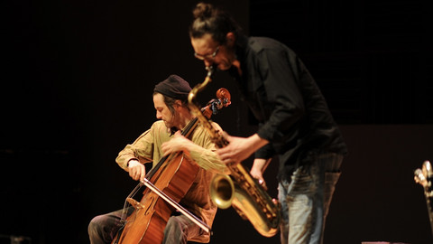 Cellist und Saxophonist musizieren gemeinsam auf einer Bühne