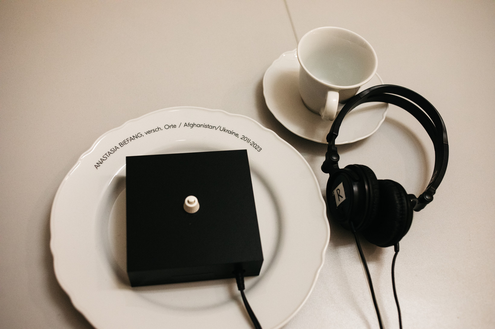 Teller und Tasse. Auf dem Teller liegt ein Kasten mit Knopf, daneben ein Kopfhörer