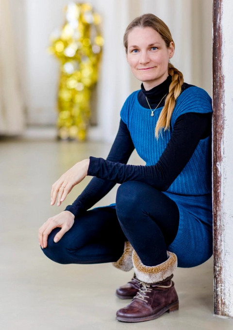 Person sitzt in der Hocke am rechten Bildschirmrand und lächelt in die Kamera