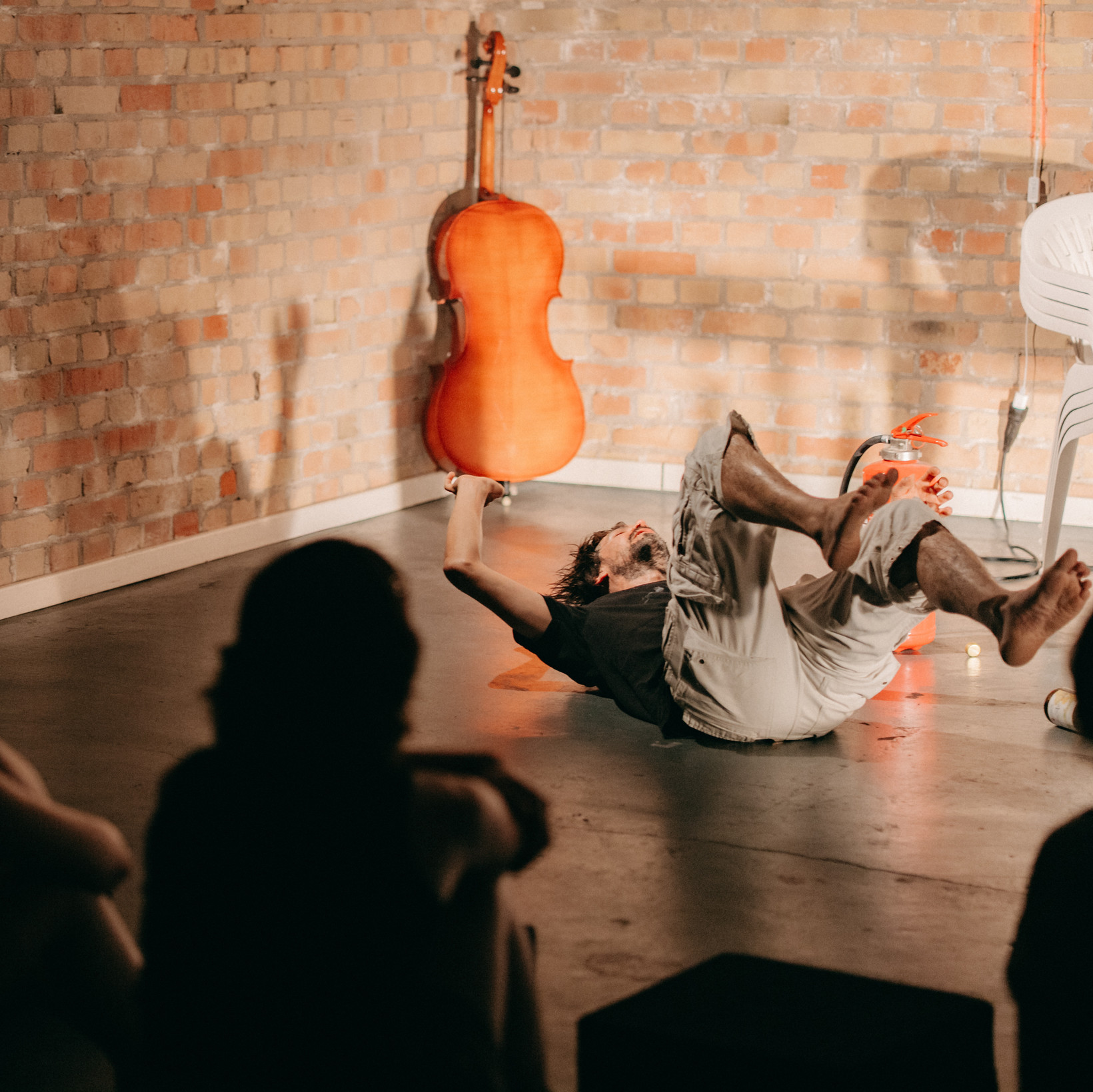 Person liegt auf dem Rücken auf dem Boden. Im Hintergrund ein Cello an der Wand