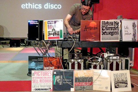 Ein Mann legt Schallplatten auf. Im Hintergrund steht "ethics disco" vor ihm stehen verschiedene Plattencover