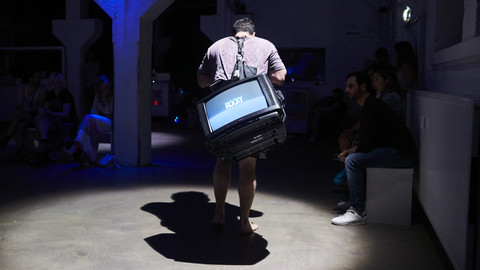 Person läuft mit einem Fernseher auf dem Rücken durch einen dunklen Raum
