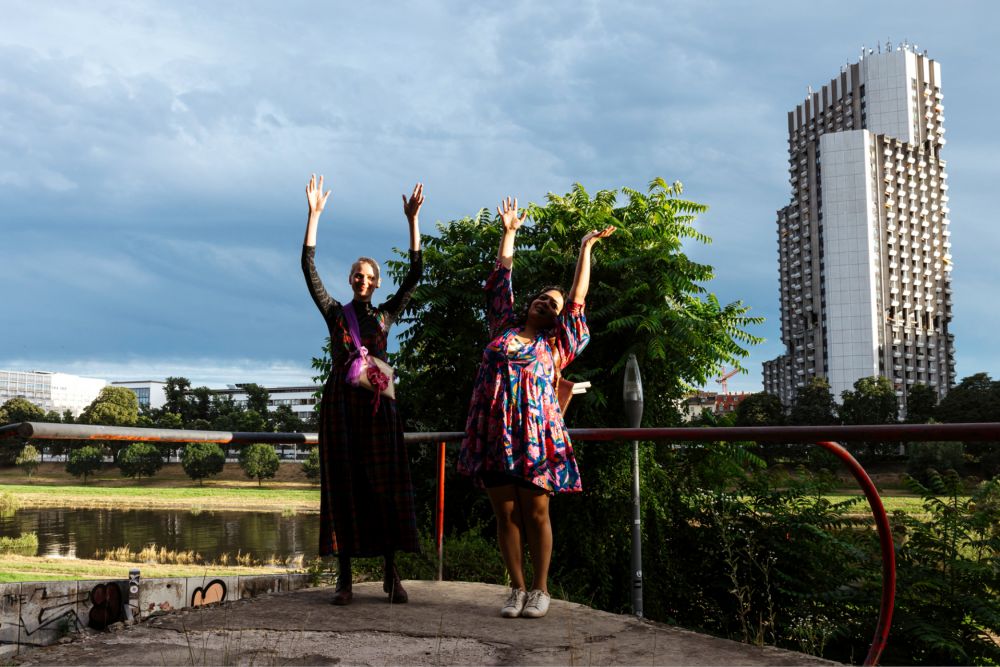 Zwei Frauen springen in die Höhe. Im Hintergrund Grünflächen und ein Hochhaus