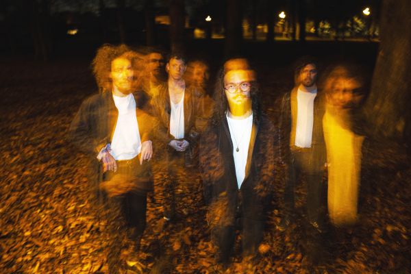 Foto von vier Männern auf einem Boden voller Herbstblätter. Das Bild ist verschwommen, der Farbton ein warmes gelb.