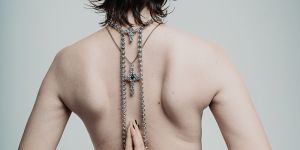 Person mit nacktem Oberkörper steht mit dem Rücken zur Kamera. Auf ihrem Rücken liegt ein Schmuck-Kreuz. Sie hat die Hände zum Gebet gefaltet. 